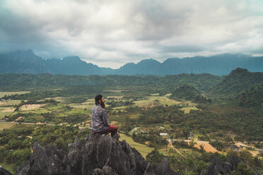 Laos, Vang Vieng, Wanderer sitzt auf einem Felsen und schaut in die Ferne - KKAF00910