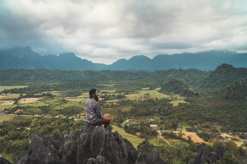 Laos, Vang Vieng, hiker sitting on rock, looking at distance - KKAF00910