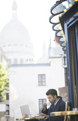 Businessman working at sidewalk cafe near Sacre Coeur Basilica, Paris, France - CAIF16331