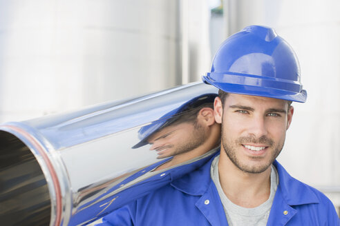 Porträt eines lächelnden Arbeiters, der ein rostfreies Stahlrohr trägt - CAIF16357