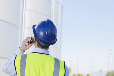 Worker talking on cell phone and looking up at silage storage towers - CAIF16359