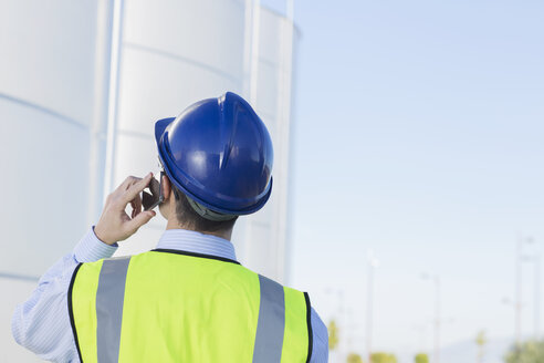 Arbeiter telefoniert mit Handy und blickt auf Silagetürme - CAIF16359