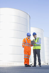 Businessman and worker using digital tablet next to silage storage towers - CAIF16380