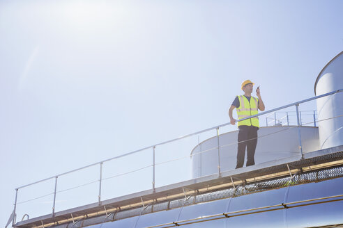 Arbeiter mit Walkie-Talkie auf der Plattform neben den Silagetürmen - CAIF16382