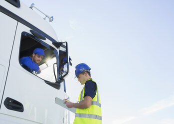 Worker with clipboard talking to truck driver - CAIF16409