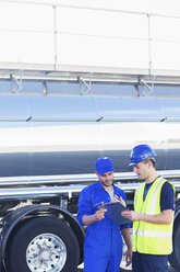 Workers with clipboard talking next to stainless steel milk tanker - CAIF16410
