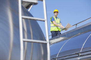 Worker using laptop on platform above stainless steel milk tanker - CAIF16416