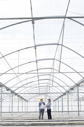 Architect and businesswoman reviewing blueprint in empty greenhouse - CAIF16475