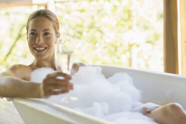 Woman having champagne in bubble bath - CAIF16563
