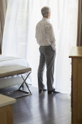 Businessman looking out window in hotel room - CAIF16612