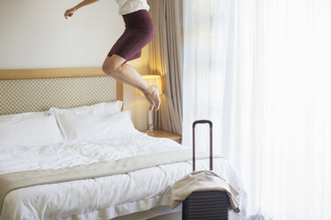 Geschäftsfrau springt auf Bett in Hotelzimmer - CAIF16625