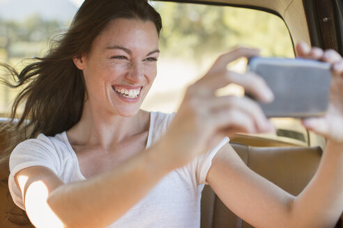 Frau fährt im Auto und fotografiert mit dem Handy - CAIF16734