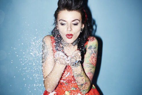 Portrait of tattooed woman blowing artificial snow - ABIF00144