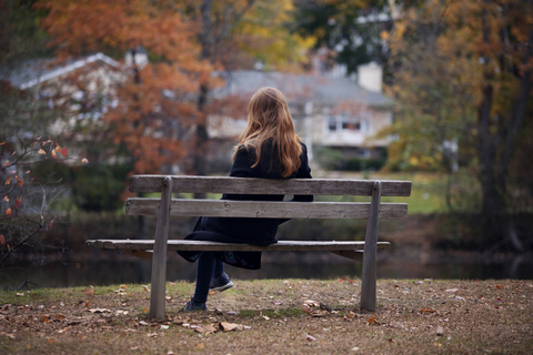 Rückansicht einer Frau, die auf einer Bank am See sitzt, lizenzfreies Stockfoto