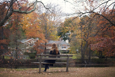 Woman sitting on bench against lake - CAVF08318