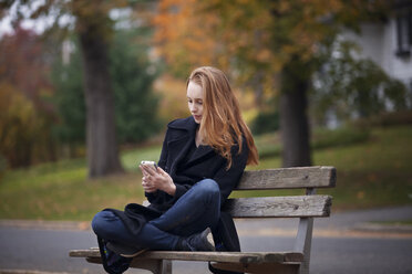 Frau benutzt Smartphone, während sie auf einer Bank sitzt - CAVF08320