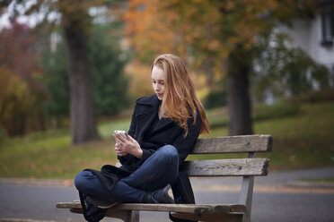 Woman using smart phone while sitting on bench - CAVF08320