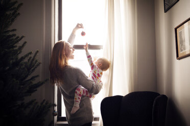 Frau, die mit ihrem kleinen Mädchen spielt, während sie zu Hause am Fenster steht - CAVF08361
