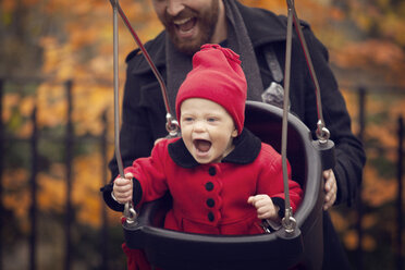 Father pushing baby girl on swing in park - CAVF08372