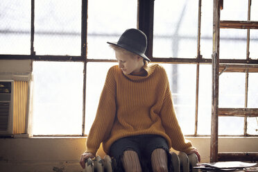 Woman looking down while sitting on radiator by window at home - CAVF08388