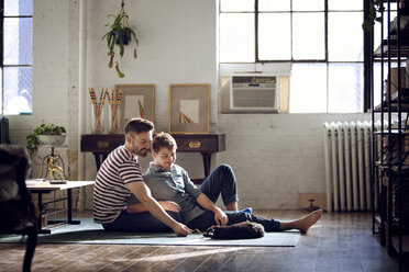 Gay couple looking at cat lying on floor at home - CAVF08393