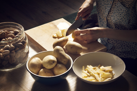 High angle view of woman cutting potatoes on cutting board at home stock photo