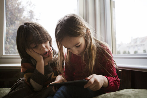 Junge schaut auf seine Schwester, die zu Hause einen Tablet-Computer benutzt - CAVF08473