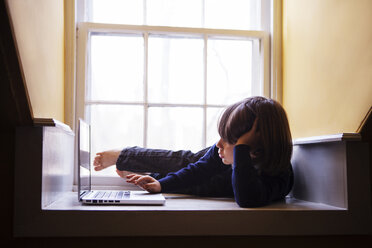 Junge benutzt einen Laptop, während er zu Hause auf dem Boden liegt - CAVF08480