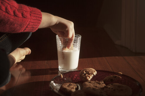 Ausgeschnittenes Bild eines Mädchens, das einen Keks in Milch eintaucht, während es auf dem Boden sitzt - CAVF08490