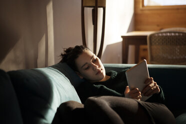 Teenage girl looking at tablet while sitting on sofa at home - CAVF08519