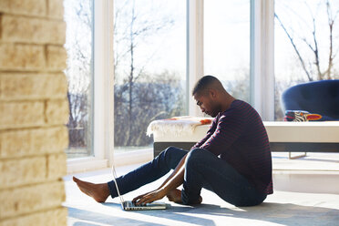 Side view of man using laptop while sitting at home - CAVF08539