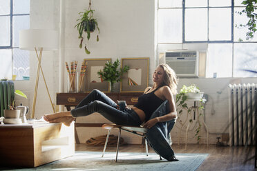 Happy woman sitting on chair at home - CAVF08573