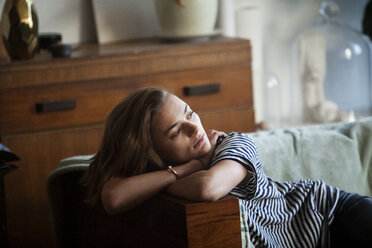 Thoughtful woman looking away while sitting on sofa - CAVF08597