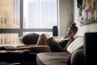 Frau liest ein Buch, während sie zu Hause auf dem Sofa sitzt - CAVF08605