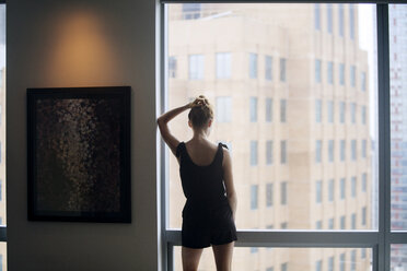 Rear view of woman standing by window at home - CAVF08608