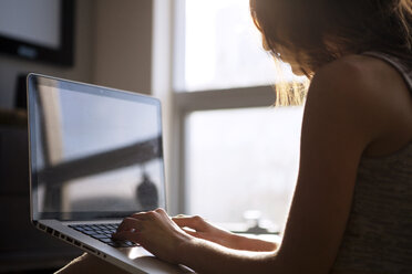 Frau benutzt Laptop, während sie zu Hause am Fenster sitzt - CAVF08619