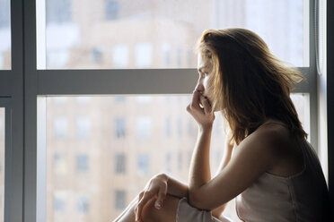 Seitenansicht einer nachdenklichen Frau, die am Fenster sitzt - CAVF08626