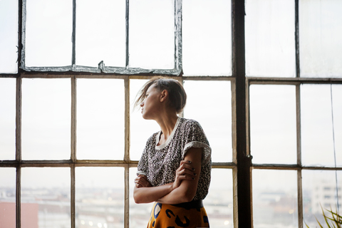 Frau schaut durch ein Fenster, während sie zu Hause steht, lizenzfreies Stockfoto