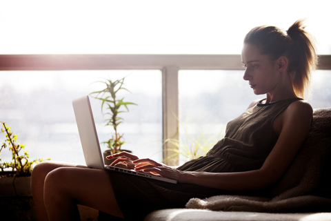 Frau benutzt einen Laptop, während sie zu Hause auf dem Sofa sitzt, lizenzfreies Stockfoto