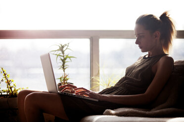 Frau benutzt einen Laptop, während sie zu Hause auf dem Sofa sitzt - CAVF08669