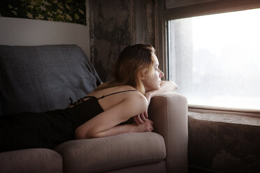 Woman looking away while lying on sofa at home - CAVF08681