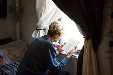 Hoher Blickwinkel der Frau, die ein Buch liest, während sie zu Hause am Fenster sitzt - CAVF08698