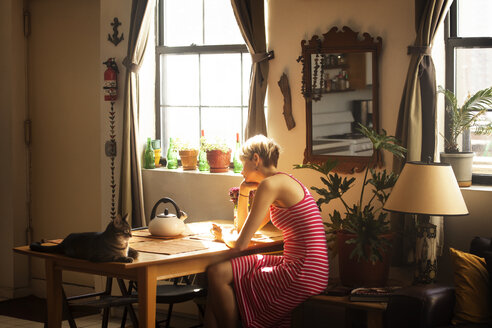 Side view of woman sitting by table at home - CAVF08708