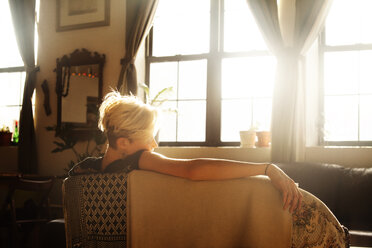 Rear view of woman leaning on sofa - CAVF08712