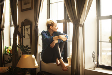 Woman looking away while sitting by window sill at home - CAVF08713