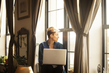 Frau mit Laptop auf der Fensterbank zu Hause - CAVF08714