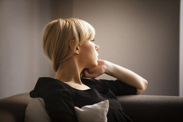 Young woman looking away while sitting on sofa at home - CAVF08723