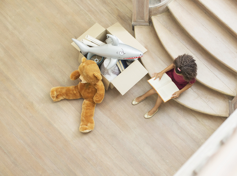 Junges Mädchen liest auf einer Treppe mit Spielzeug, lizenzfreies Stockfoto
