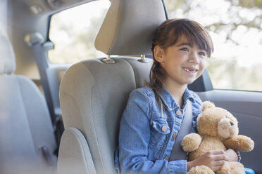 Glückliches Mädchen mit Teddybär auf dem Rücksitz eines Autos - CAIF16909