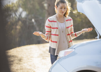 Frustrated woman looking at car engine at roadside - CAIF16918